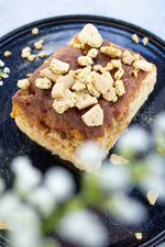 cinnamon biscuit with crumbly topping on a dark plate with white flowers in the background