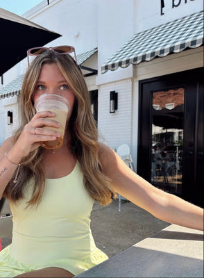 Woman in a yellow dress drinking from a coffee cup outdoors.