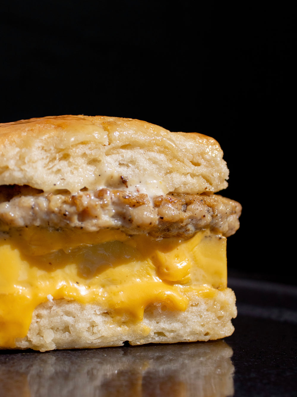 Biscuit sandwich with chicken sausage and cheese on a reflective surface with a black background