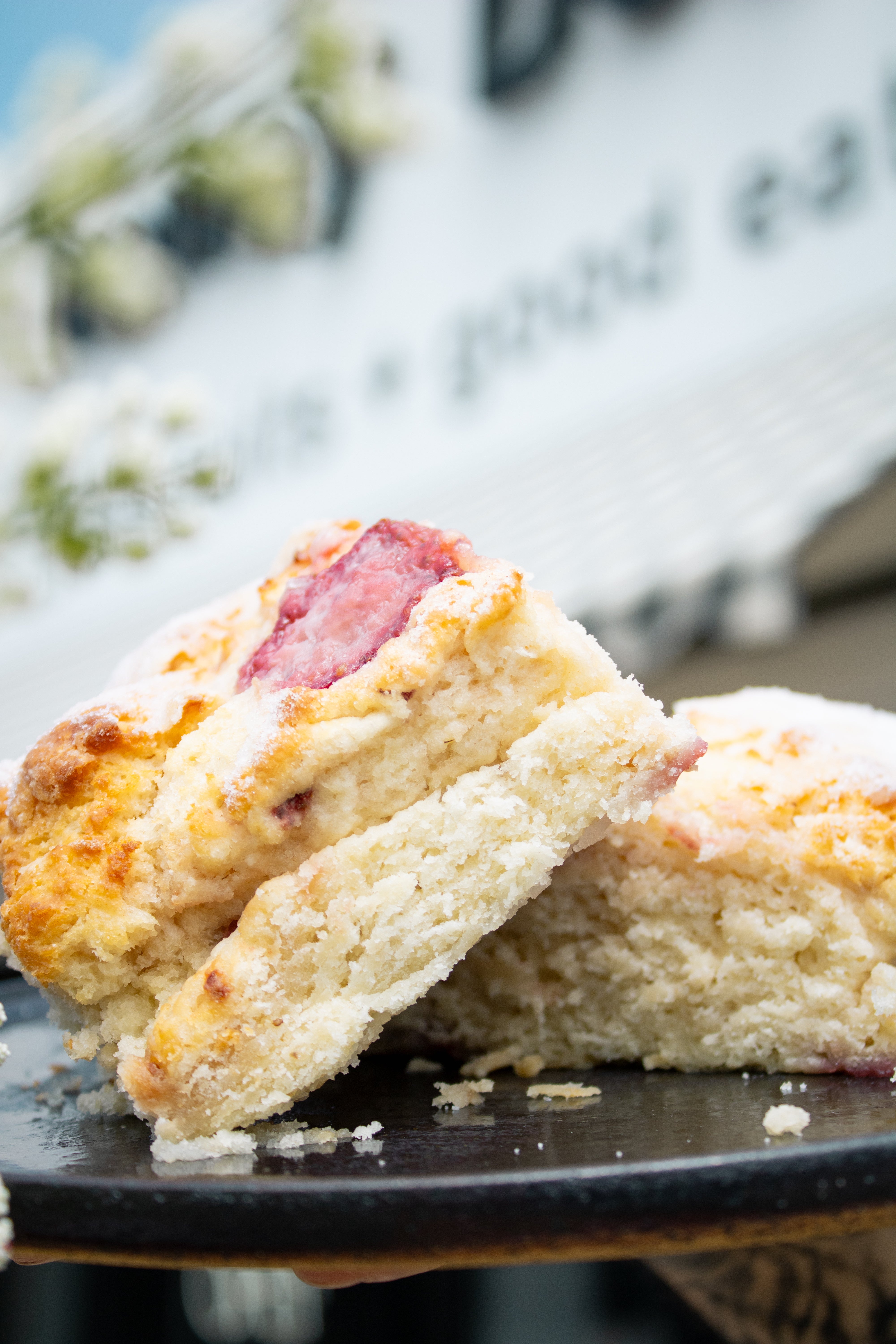 Two strawberry biscuits on a black plate with a blurred outdoor background
