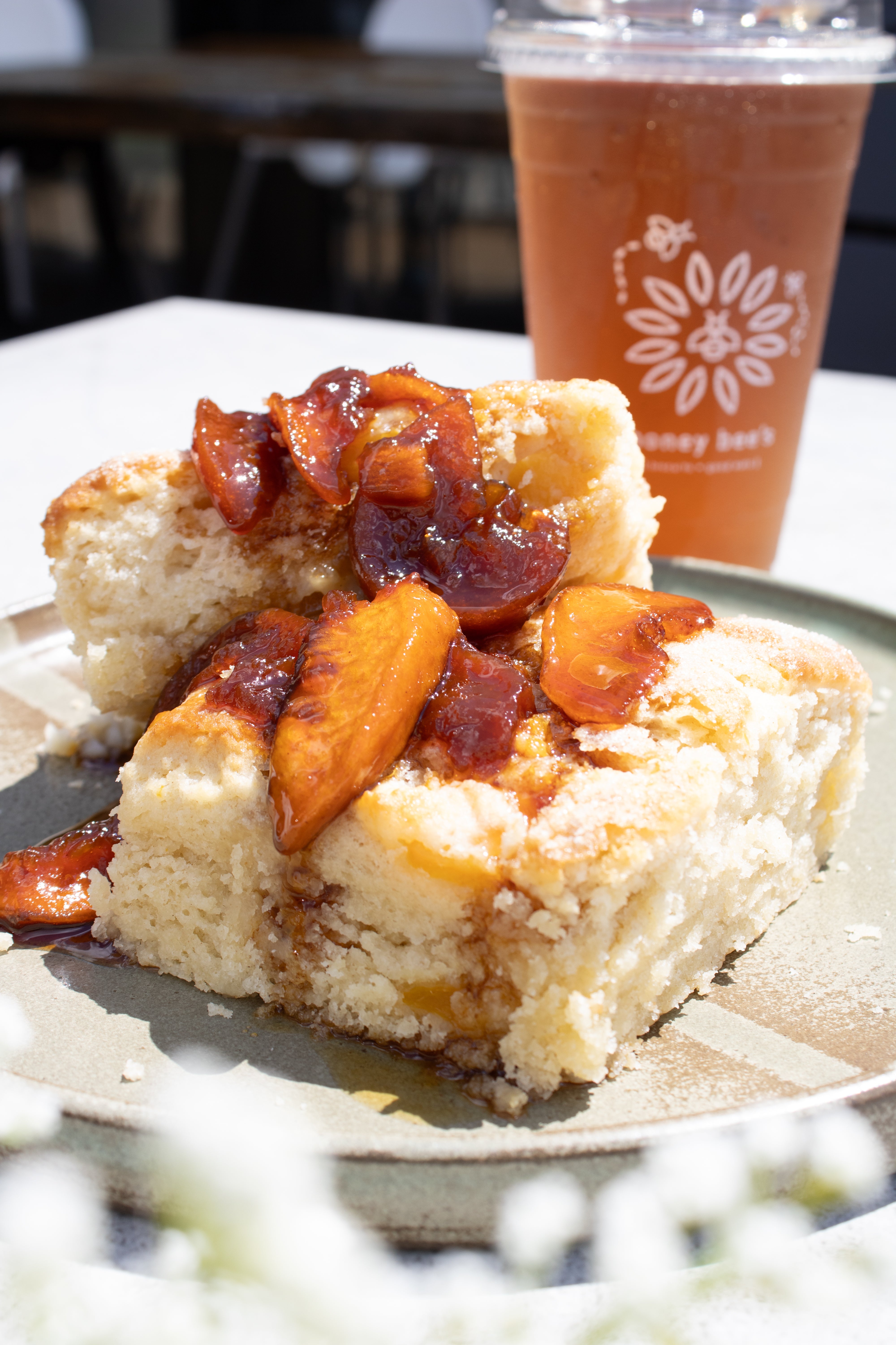 Two biscuits with peach compote on a plate, accompanied by a drink with a logo in the background