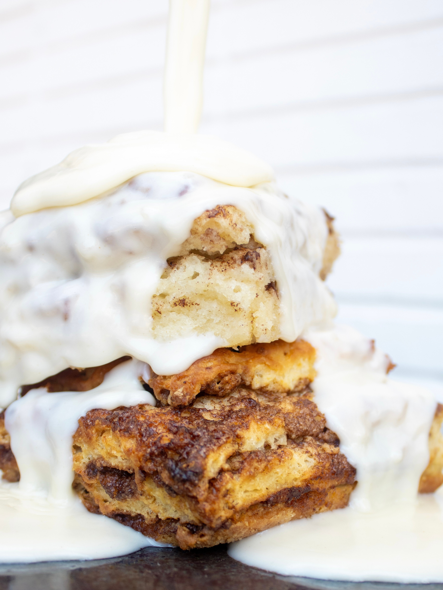 Cinnamon roll biscuit with sweet cream gravy being drizzled over it on a white background