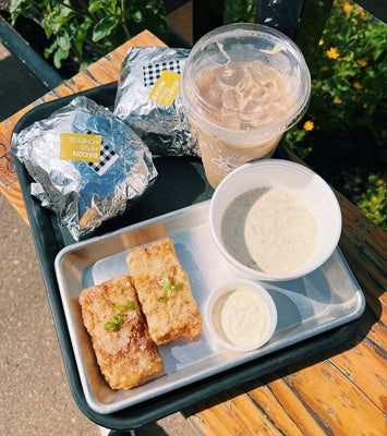 Tray with food items including a drink, snacks, and a bowl on a wooden table outdoors.